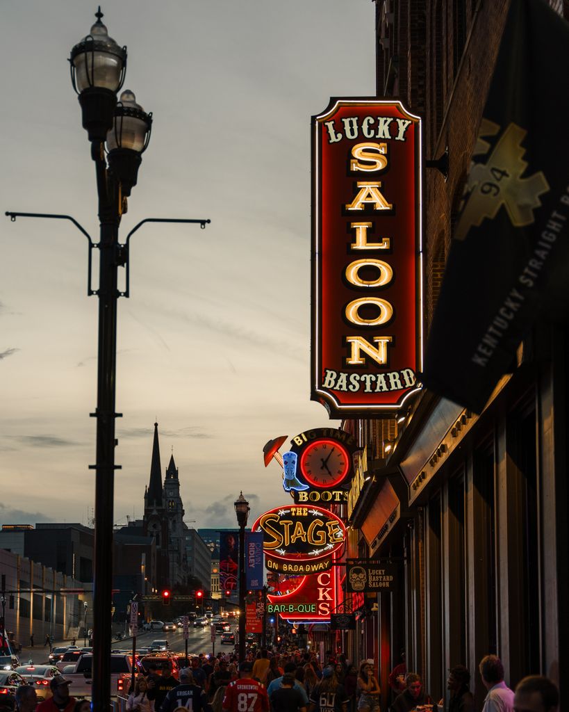 A bustling urban street with neon signs in Nashville, Tennessee at dusk.